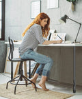 Woman using Heavy Duty Adjustable Table Leg Extenders at a desk, highlighting ergonomic design and adjustable heights.