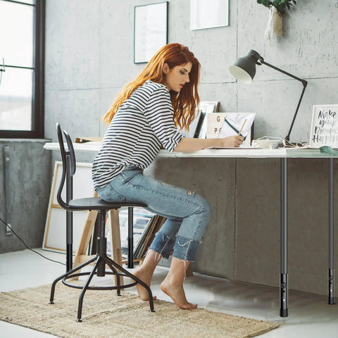 Woman using Heavy Duty Adjustable Table Leg Extenders at a desk, highlighting ergonomic design and adjustable heights.