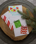 Christmas cards with festive designs on a wooden platter surrounded by pine branches.