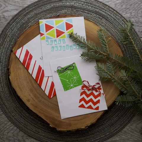 Christmas cards with festive designs on a wooden platter surrounded by pine branches.