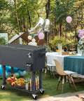 80 Quart Rolling Ice Chest Cooler Cart for Patio and Poolside Parties with drinks on lower shelf, set outdoors.