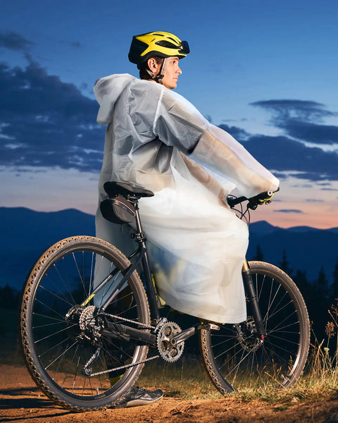 Cyclist wearing a 14 Pack Reusable EVA Rain Ponchos for Adults with Drawstring Hoods Waterproof Rain Gear in white at dusk