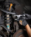 Side view of GearWrench Ball Joint Separator 3916D in use on a vehicle suspension; orange handle and silver fork.
