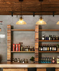 Bar scene with three pendant lights, industrial design and amber glow illuminating wooden shelves stocked with liquor and brick pillars.