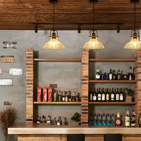 Bar scene with three pendant lights, industrial design and amber glow illuminating wooden shelves stocked with liquor and brick pillars.