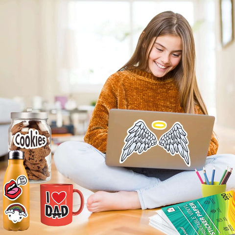 Premium printable vinyl sticker paper pack with green packaging on desk; laptop features angel-wing sticker.