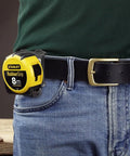 Person wearing jeans with tape measure clipped to belt using Sturdy Tape Measure Holder And Drill Holster With Belt Clip Hands Free Tool Pouch For Measuring Tapes Impact Drivers And Any Hooked Tool Heavy Duty ABS Construction With Reinforced Stainless Steel Clip.