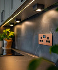 Modern Screwless Double Switched Wall Socket In Polished Copper mounted above a kitchen countertop with stylish lighting.