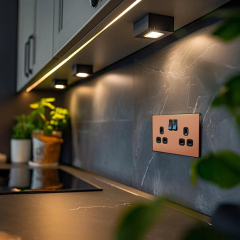 Modern Screwless Double Switched Wall Socket In Polished Copper mounted above a kitchen countertop with stylish lighting.