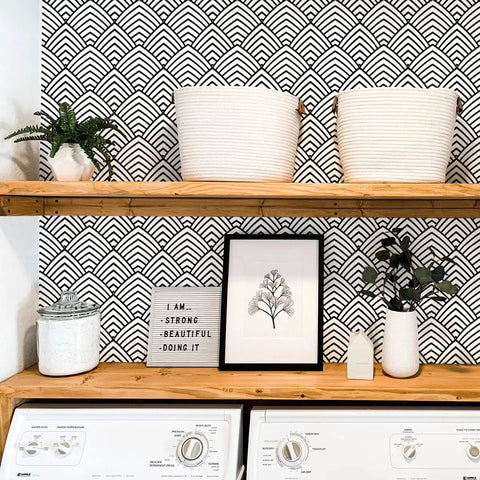 Laundry room with black and white peel and stick wallpaper with geometric chevron and herringbone pattern on wall behind wood shelves