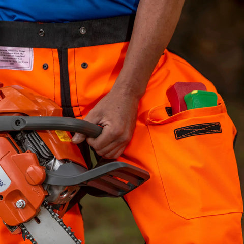 Person holding chainsaw wearing Hi Vis Safety Orange Apron Style Chainsaw Chaps Type A Frontal Protection 5 Layer Chain Stopping