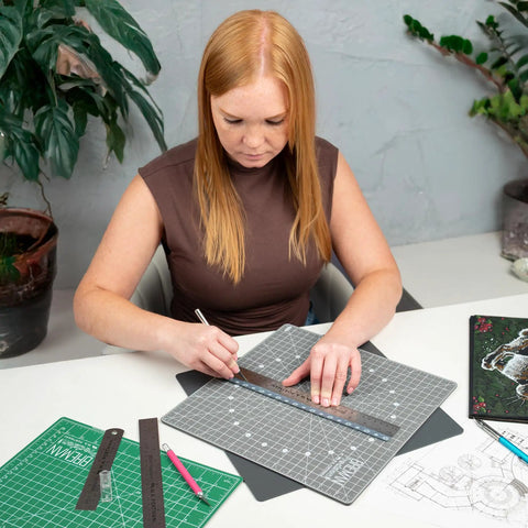 Person using Stainless Steel Ruler Set Three Pack With One 6 Inch And Two 12 Inch Metal Straight Edges for drawing on a desk