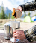 Person preparing coffee with Camper's Percolator Coffee Pot For Camping 9 Cup Aluminum Brew Coffee Pot outdoors.