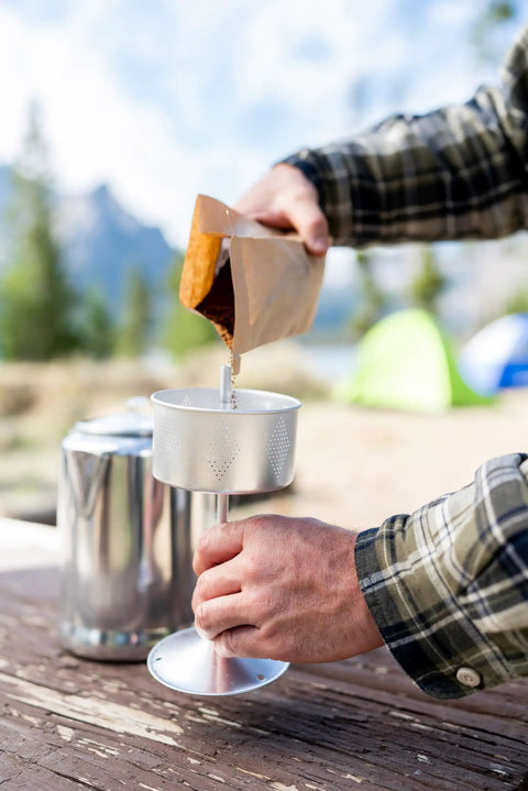 Person preparing coffee with Camper's Percolator Coffee Pot For Camping 9 Cup Aluminum Brew Coffee Pot outdoors.