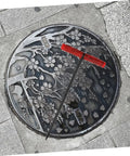 Badass Heavy Duty Steel Manhole Cover Lifter Hook Built With A Nifty T Handle resting on a decorative manhole cover.