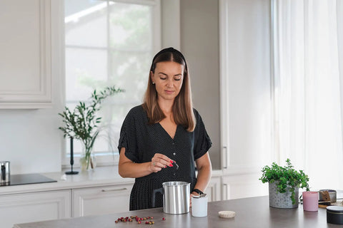 A woman using the Premium Soy Candle Making Kit Full Set With Soy Wax 7 Oz Jars And Tins, crafting candles at a kitchen counter.