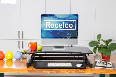 32 Inch Height Adjustable Standing Desk Converter With Slide Out Keyboard Tray and Dual Monitor Riser on a wooden table with decor.