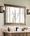 Bathroom with large wooden mirror, two wall sconces, and modern faucet above a wooden vanity.