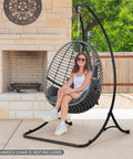 Woman sitting in egg chair on black Heavy Duty Hammock Chair Swing Stand Outdoor Frame Holds Up To 400 Lbs Black Sturdy Triangle Design All Weather Powder Coated Steel For Backyard Deck Or Patio Chill Vibes And Relaxation on patio.