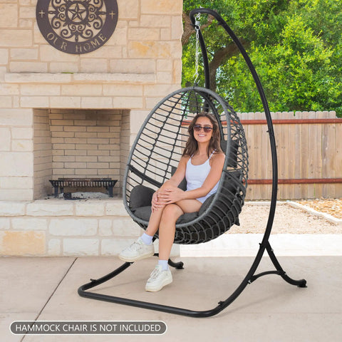 Woman sitting in egg chair on black Heavy Duty Hammock Chair Swing Stand Outdoor Frame Holds Up To 400 Lbs Black Sturdy Triangle Design All Weather Powder Coated Steel For Backyard Deck Or Patio Chill Vibes And Relaxation on patio.