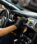 Hella Durable Black Nitrile Safety Gloves With Sick PyraGrip Texture For Superior Traction On Greasy Jobs Heavy Duty Industrial Gear being used by a person cleaning a car interior.