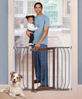 Walk Through Baby And Pet Gate With Walnut Wood And Charcoal Metal Accents in doorway with dad holding toddler, dog sitting nearby
