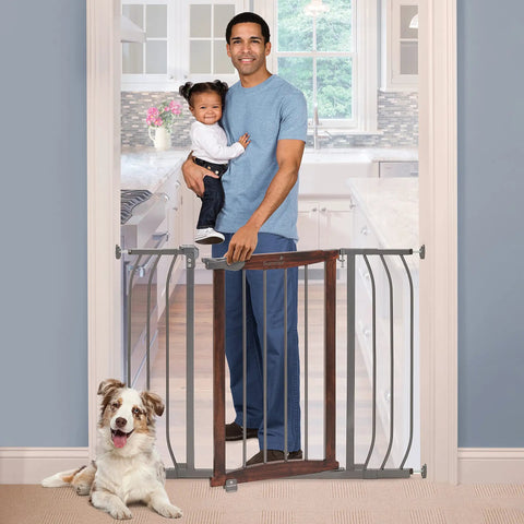 Walk Through Baby And Pet Gate With Walnut Wood And Charcoal Metal Accents in doorway with dad holding toddler, dog sitting nearby