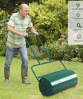 Man uses 24 Inch Tow Behind Lawn Roller With 13 Gallon Water Or Sand Fill U Shaped Handle Easy Push Or Pull Setup for seed bedding in garden.