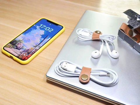 Leather Cord Organizer And Cable Keeper Case For Earbuds And Headphones on a desk with smartphone