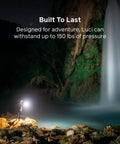 Hiker using Luci Original Solar Inflatable Camping Lantern With USB C Recharge by waterfall at night, showcasing durability.