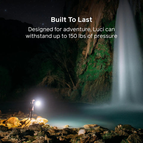 Hiker using Luci Original Solar Inflatable Camping Lantern With USB C Recharge by waterfall at night, showcasing durability.