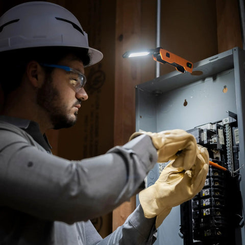 Electrician using foldable handheld work light with 500 lumen LED USB C rechargeable, attached via magnetic base, in a service panel.