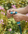 Person using medium duty thumb control garden hose nozzle with adjustable spray pattern in a garden