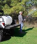 Person using Beefy 4.0 GPM 12V Diaphragm Pump with Half Inch NPT Ports to spray in a field, attached to a utility vehicle.