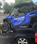 Beefed Up Heavy Duty Wheel Chock Tie Down Kit With 4500 Lb Break Strength, securing a blue ATV on a trailer.