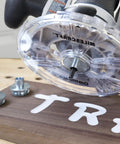Universal 7 Inch Router Base Plate With Adjustable Swivel Wings And Clear Top For Sharp Vision shown on a wooden surface with centering pins.