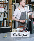 Barista setting up Wooden Coffee Station Organizer For Countertop With White Finish Farmhouse Style Coffee Bar Holder And K Cup Pod Storage Basket With Handle Premium Pine Wood Perfect For Mugs Pods Creamers And Syrups on coffee shop counter