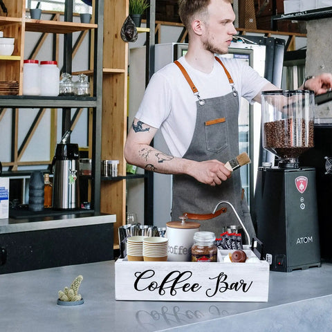 Barista setting up Wooden Coffee Station Organizer For Countertop With White Finish Farmhouse Style Coffee Bar Holder And K Cup Pod Storage Basket With Handle Premium Pine Wood Perfect For Mugs Pods Creamers And Syrups on coffee shop counter