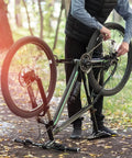Person adjusting 6/7/8 Speed Bike Chain for Road and Mountain Bikes, Pro Grade Performance, outdoors with fallen leaves.