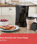Black Compact Brew And Go Personal Coffee Maker With Travel Mug on kitchen counter next to toast and berries