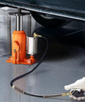 Orange air-hydraulic bottle jack 20-ton installed under a vehicle with air pump and control hose