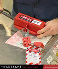 Heavy Duty 220 Volt Cord Lockout For Two Plugs Large Electrical Plug Lockout Device Industrial Grade Non Conductive Polypropylene OSHA Compliant Red Lockout Tool For Energy Isolation in use on a workbench by a person securing two plugs with danger tag visible.
