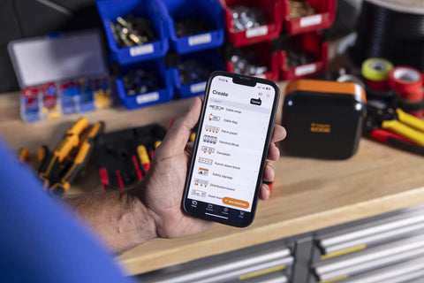 Portable Industrial Label Printer With Bluetooth And Pro Label Tool App Hands Free Belt Clip For Tight Jobsite Spaces Rechargeable Battery Prints Durable Labels Up To 1 Inch Industrial Formats, in use on a workbench.