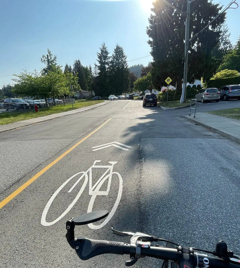 Big Bar End Mirror For E Bikes With Automotive Grade Glass Delivers Crystal Clear View On Left Or Right Fits Most 14.8 To 23 Mm Handlebars Wide Opening No Glare Blast Resistant Safety Mirror For Your Ride featuring a handlebar view on a sunny road with clear bike lane marking.