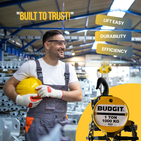 Front view of Budgit 1-ton air hoist with chain, yellow finish, in factory with worker holding hard hat.