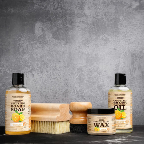 Cutting Board Oil With Lemon And Orange Oils Food Grade Mineral Oil For Cutting Boards And All Wood Surfaces Keeps Your Boards Looking Fresh Restores And Protects Butcher Block Nourishing Conditioner 12 Oz bottle with cleaning brush and wax jar on grey background.