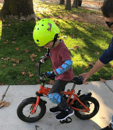 Child wearing green helmet with Kid Friendly Knee And Elbow Pad Set With Pro Grade Bike Gloves for Ages 2-11 on balance bike