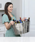 Smiling person holding an Aspen Heavy-Duty Oval Stainless Steel Drink Cooler For Parties 25-Quart Large Ice Bucket in a kitchen.