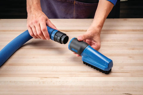 Person using Dust Right Click-Connect Bench Brush And Dock Kit Heavy Duty Soft Bristle Cleaning Tool with FlexiPort hose on wooden bench.