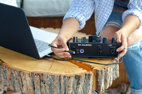 Person setting up USB-C Audio Interface Kit With 2 In 2 Out connected to a laptop on a wooden table